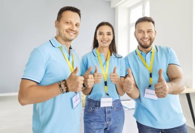Mavi tişörtlü bir grup genç gönüllü baş parmaklarını kaldırıp kameraya bakıyorlar. Yardım merkezinde çalışan olumlu kadın ve erkekler, insani yardım ve yardım sağlıyorlar..