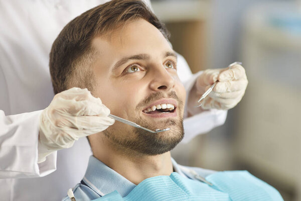 Portrait of young smiling man patient having teeth examined by dentist doctor using dental instruments, ensuring proper oral care during regular medical check up in dentistry clinic. Oral health.
