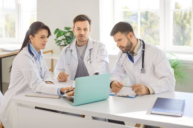 Doktorlar, klinikteki çalışma masasında dizüstü bilgisayarla oturup tanı koyma, test sonuçlarını kontrol etme ya da tedavi planlama konularını tartıştılar. Sağlık personeli, sağlık ve takım çalışması kavramı.