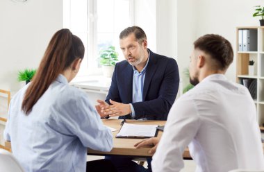 Aile çifti bir emlakçı ya da emlak danışmanıyla ofiste bir toplantı sırasında iletişim kuruyor. Profesyonel etkileşim müşteri hizmetleri ve mülkiyet tartışmalarını vurgular.