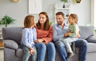 Mutlu, genç bir aile birlikte kanepede oturup neşeli oğlanı dikkatle dinliyor. Pozitif oğul, anne, baba ve kız kardeşiyle günün haberlerini paylaşıyor, ilginç bir şey anlatıyor. Aile bağları kavramı.