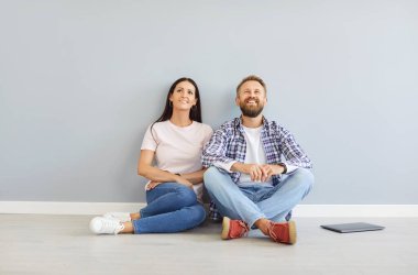 Yeni evin boş odasında oturan mutlu genç bir çiftin portresi. Dizüstü bilgisayarlarıyla taşınma ve taşınma gününün keyfini çıkarıyorlar. Taşınmak, kira, gayrimenkul ve konut kredisi.