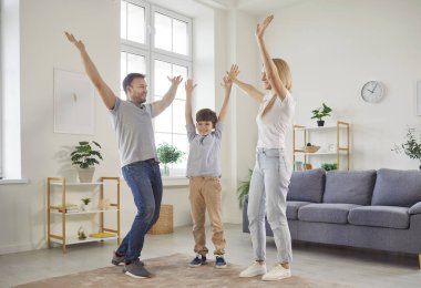 Mutlu bir aile, şefkatli bir anne, baba ve küçük bir oğul, çocuklu bir aile evde eğleniyor, modern oturma odasında yeni bir daireye taşındıktan sonra kahkahalarla gülüyor, birlikte vakit geçiriyorlar.