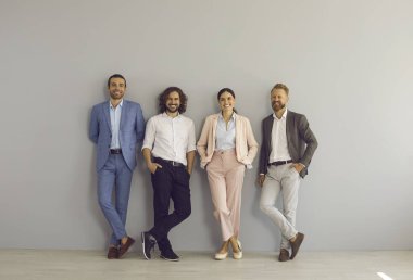 Resmi ve şık giyimli dört başarılı iş adamının toplu portresi. Gri stüdyo ya da ofis duvarının yanında birlikte duran 4 mutlu meslektaştan oluşan bir ekip ya da profesyonel yönetici.