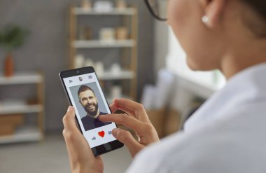 Kadın akıllı telefon ekranındaki mobil flört uygulamasında erkeklere benzer bir fotoğraf verecek. İnternette aşk ve ilişki arayan bekar bir kadın. Sosyal uygulama kavramında romantik partner aranıyor.