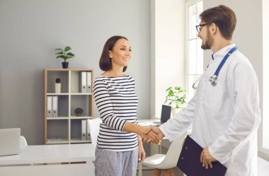 Modern klinikte ya da hastanede gülümseyen mutlu bir hasta tıp uzmanıyla el sıkışıyor. Dost canlısı doktor, olgun bayanı ofisinde karşılıyor. Sağlık hizmetleri, sağlık kontrolü, doktor konseptine ziyaret