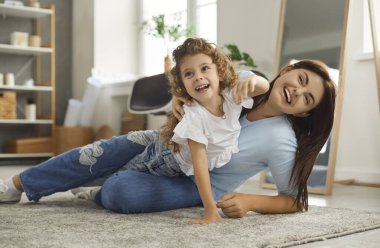 Mutlu küçük anne ve küçük çocuk birlikte eğleniyorlar. Neşeli gülümseyen anne ve sevimli kız evdeki halının üstünde, modern oturma odasında, yer altı ısıtmalı oynuyorlar. Aile, eğlence, aşk konsepti