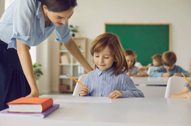 Sınıftaki ilkokul öğrencisi bir bayan öğretmenin yardımıyla bir okul ödevi yapar. Dost canlısı öğretmen, genç öğrencilerine öğretmekten ve onlara yardım etmekten mutluluk duyar. Eğitim kavramı.