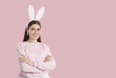 Pembe fotokopi çekilen mutlu Paskalya tavşanı kızları. Pastel pembe kazak, küpeler ve komik tavşan kulakları takan güzel bir kadın. Kolları pembe fotokopi arka planında katlanmış duruyor.