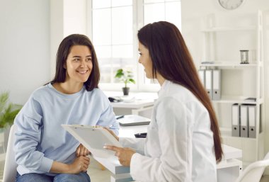 Hasta ile arkadaş canlısı bir kadın. Gülümseyen kadın doktor hastayla konuşur ve muayene sırasında karta notlar alır. Genç tatmin olmuş kadın, reçetesini yazan doktoru dinler..