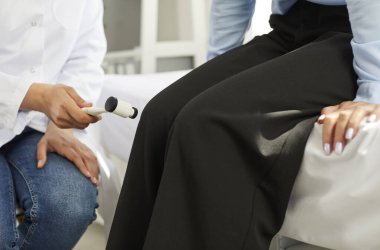 Doktor hastayı muayene ediyor. Profesyonel nörolog derin tendon reflekslerini test ediyor, elinde çekiç tutuyor ve genç kadının refleksini kontrol ediyor. Kesilmiş atış. Sağlık, nöroloji, tıbbi kontrol kavramı