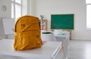 Okul sınıfı. Sınıftaki öğrenci masasında yeni okul çantası. Büyük, sarı bir sırt çantası, büyük, modern bir sınıfın tahtasında, masanın üzerine yerleştirilmiş. Okul konseptine dönelim.