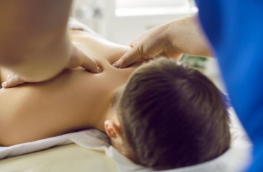 Erkek masör ellerinin genç bir adama sağlıklı osteopatik vücut masajı yapması. Profesyonel erkek masör masaj salonundaki erkek hastanın boynuna masaj yapıyor. Seçici odak.