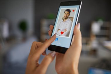 Akıllı telefondaki sohbet butonuna basan kadın aşkı ve internet bağlantısını bulmak için flört uygulamasını kullanıyor. Ekrandaki yakışıklı adam profili fotoğrafına odaklan. Modern yaşam tarzı ilişkisi, uzak ilişki