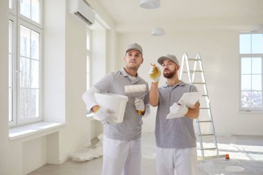 Üniformalı iki profesyonel ressam yeni apartman yenileme planını tartışıyor. Erkek müteahhit işçiler tasarım projesi hakkında konuşuyor. Ev geliştirme ve iç dekorasyon kavramı.