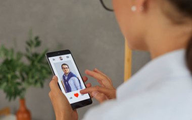 Bekar bir kadın aşkı bulmak için akıllı telefon kullanır. Cep telefonunda flört uygulaması kullanan, kullanıcı fotoğrafları aşıran ve kırmızı düğmeye basan bir kadın. Akıllı telefonu açık profilli bir şekilde kapat. Seçici odak.