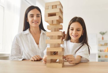 Neşeli, mutlu bir annenin portresi. Evdeki oturma odasında oturan genç kızıyla ahşap yapı taşlarıyla oynuyor. Aile eğlencesi ve insan konsepti.