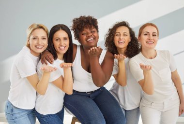 Gri arka planda yan yana duran ve hava öpücüğü veren beş farklı genç kadın, herkese sevgilerini yolluyor, iyi dostça ilişkiler kuruyor, stüdyo duvarına yapışık. 