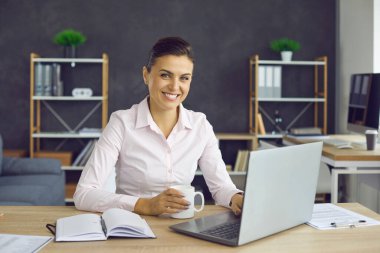 İşe başlamak için bir fincan güzel kokulu kahve. İş yerinde elinde bardakla oturan mutlu ve başarılı bir iş kadınının portresi. Ofiste dinlenen bir kadın.