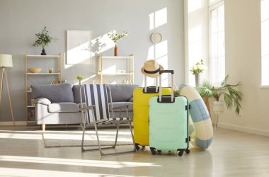 Renkli bavullar, şezlong, ve evdeki boş bir odada kauçuk yüzük standı, bavulları simgeliyor, yaz tatiline hazırlık. Seyahat heyecanı ve yolculuk beklentisi.