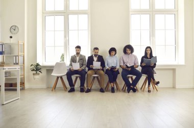 Özgeçmişi ve özgeçmişi olan bir grup erkek ve kadın aday iş görüşmesi için sırada bekliyor. Sandalyede oturan, elinde belgelerle resmi toplantıya hazırlanan beş kişi. İstihdam, iş kavramı