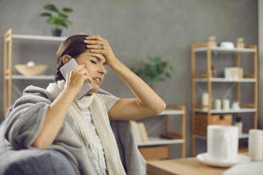 Grip ya da soğuk algınlığı geçiren mutsuz genç bir kadın doktor çağırıyor. Sıcak battaniyeye sarılı hasta kadın ya da evdeki kanepede oturan, sıcak alnına dokunan ve doktorunu arayan ekose kadın.