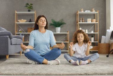 Sakin, genç, beyaz bir anne ve 7 'nin kızı Mudra elleriyle yerde oturup meditasyon yaparak negatif duyguları hafifletiyor. Rahatlamış anne ve küçük kız çocuk istirahati birlikte yoga yapıyorlar. Stressiz konsept.