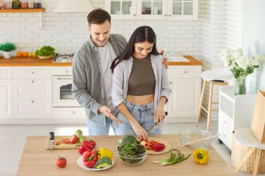 Mutlu gülümseyen genç bir çiftin portresi taze sağlıklı vejetaryen salatası ve modern mutfakta birlikte duran bir sürü sebze hazırlıyor. Vejetaryen yiyecekler, diyet ve beslenme konsepti.