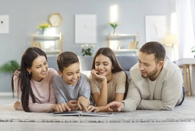 Oturma odasında halıya uzanmış eski fotoğraf albümüne bakarken mutlu bir ailenin portresi. Gülümseyen ebeveynler ve çocuklar eski günleri yad ediyorlar, anılarını paylaşıyorlar, sıcak ve neşeli bir bağ kuruyorlar..