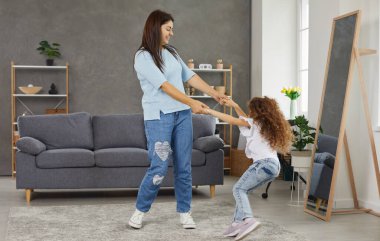 Mutlu bir aile oyunu ve evde eğleniyor. Neşeli genç anne ve neşeli küçük çocuk el ele tutuşuyor, dans ediyor ve modern tasarım ve rahat kanepe ile oturma odasında pozitif duyguların tadını çıkarıyor.