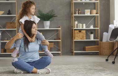 Mutlu anne ve çocuk evde. Pozitif, genç bir anne ve hoş, tatlı, güler yüzlü küçük bir kız, şık bir oturma odasında yerde otururken yana bakıyor. Aile, ev, konfor konsepti