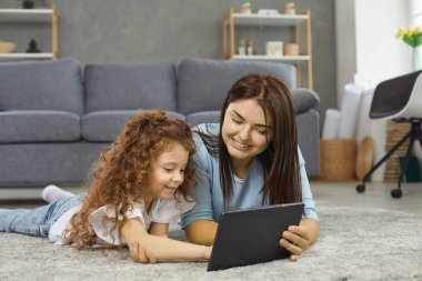 Modern teknoloji. Genç anne ve kızı evdeki sıcak zeminde birlikte yatarken dijital tablet kullanıyorlar. Boş zamanlarında izlemek için film ya da çizgi film seçerken aile internette sörf yapıyor..