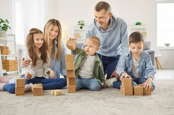 Beş çocuklu mutlu bir aile, şefkatli bir anne, baba, evde tahta bloklar oynayan üç çocuk, yerde oturup birlikte vakit geçiren çocuklar, birlikte eğlenen sevgi dolu ebeveynler.