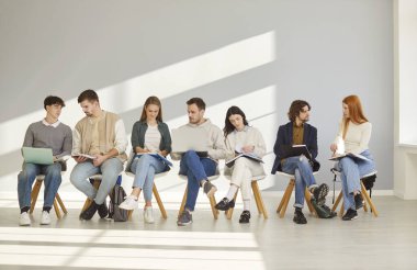 Bir grup insan koltuklarda oturuyor ve röportaj için bekliyor, iş yeri adayı oluyorlar, birbirleriyle bir şeyler tartışıyorlar, dizüstü bilgisayarlarla ve defterlerle poz veriyorlar.