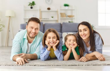 Gülümseyen dört çocuklu mutlu bir aile. İki kız ve erkek çocuk evde yerde yatıyorlar ve kameraya neşeli görünüyorlar. Çocuklu ebeveynlerin portresi. Aile zamanı ve eğlence konsepti.