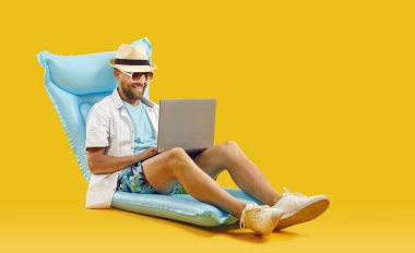 Şişme şiltede dizüstü bilgisayarla otururken deniz bileti arayan ve otel rezervasyonu yapan mutlu bir adam. Turuncu arka planda kumsalda bin yıllık adam bilardo şiltesinde oturuyor ve dizüstü bilgisayarında daktilo yazıyor..