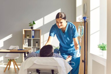 Genç, dost canlısı hemşire hasta adama klinikte serum ve vitamin terapisi almasında yardım ediyor. Kadın doktor, erkek hastasına danışmanlık yapıyor. Hastanede kanepede yatıyor..