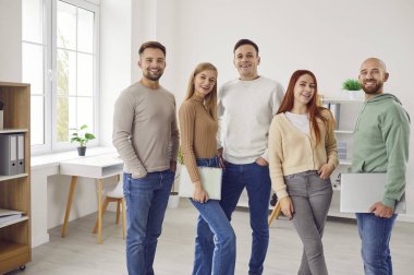 Bir grup genç kadın ve erkek kameraya bakıyor ve ofiste gülümsüyor. Çalışanların takımı, şirket çalışanları ya da bir grup öğrencinin güvenli ve neşeli bir şekilde sıraya girmesi..