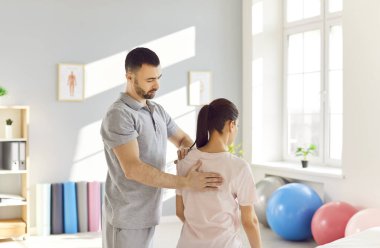 Doktor Osteopath rehabilitasyon kliniğindeki hastayı muayene ediyor. Genç erkek fizyoterapist kadının sırtında tedavi uyguluyor. Kayropraktik uzmanı omurga eğriliği ve sırt ağrısı olan kadınlara yardım ediyor..