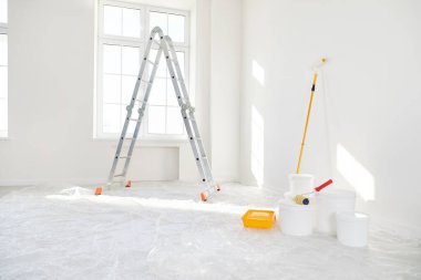 Basamaklı merdiven, yeni evdeki boş ışık odasında duran boya silindirli kovalar ya da yeni boyanmış beyaz duvarları olan bir daire. Evdeki yenileme işlemi. Ev onarımı ve taşınma günü konsepti.