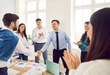 İki adam buluşmayı bitirip el sıkışıyor ve anlaşma yapıyor, iş başarısı ya da iş yeri sözleşmesi imzalıyor. Bir grup iş adamı iş arkadaşlarını alkışlıyor..