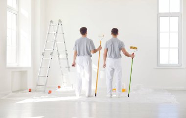 Arkada duran erkek ressamlar, boya fırçasıyla duvarları boyayan inşaat işçileri, koruyucu üniforma giyen profesyonel servis ekibi odaları tamir ediyor.