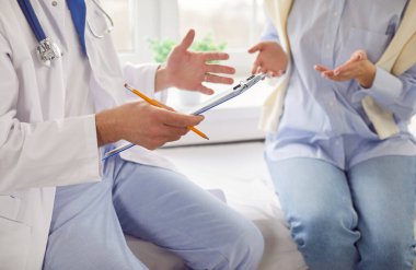 Steteskoplu beyaz üniformalı terapist doktor ve klinikteki kadın hasta konuşuyor, hasta kadın tıbbi test sonuçlarını, muayene sonuçlarını, klinikte tıbbi hizmeti, sağlık hizmetlerini kapatıyorlar.
