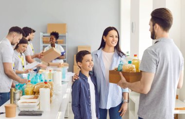 Ailesinin kâr amacı gütmeyen bir kuruluştan yiyecek yardımı alması gerekiyor. Erkek gönüllü, mutlu bir kadın ve oğluna bir kutu erzak veriyor. Yardım, mülteciler, yoksulluk, sosyal yardım, gıda bağışı konsepti