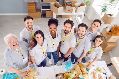 Kar amacı gütmeyen bir organizasyonda çalışan çeşitli gönüllülerden oluşan bir ekip. Yüksek açılı grup portresinden üniformalı çok ırklı mutlu insanları yemek yardımı olan bir masada resmettiler. Sadaka, bağış konsepti.