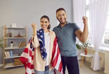 Mutlu gülümseyen Amerikan halkı, kazanan jest yapıyor, omuzlarında ABD bayrağı taşıyan bir kadın. Vatansever gülümseyen çift, bayramı kutluyorlar, Amerikan Vatanseverlik Günü, ülke gururu