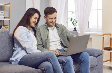 Genç, mutlu aile çifti evde boş zamanlarını birlikte geçiriyorlar. İnternette bilgisayar kullanıyorlar, internet eğlencesine katılıyorlar, kanepede oturuyorlar. Gülüyorlar, gülüyorlar, birlikte eğleniyorlar..