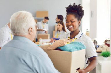 Fakir insanlar sosyal yardım alıyorlar. Yardımsever, güler yüzlü Afrikalı Amerikalı gönüllü kız, ihtiyacı olan yaşlı adama sürdürülebilir yeniden kullanım için ikinci el giysi kutusu veriyor. Bağış, bağış konsepti.