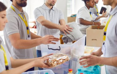 İnsani yardım merkezinde çalışan gönüllüler. Çeşitli Kafkasyalı ve Afrikalı Amerikalı erkek ve kadınlar, mülteci barınaklarındaki insanlara götürmek için yiyecek ve giyecek topluyorlar. Yardım, yardım, bağış konsepti
