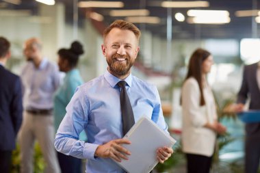 Resmi giysiler içinde gülümseyen, kendine güveni tam genç bir iş adamının portresi. Ofiste çalışan şirket çalışanlarından oluşan bir ekiple kamera karşısında neşeli görünüyor. İş portresi kavramı